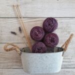 A captivating still life of purple yarn balls with knitting needles in a rustic container.